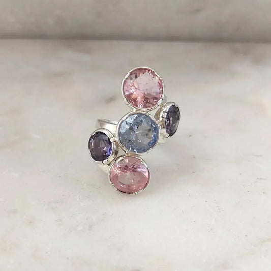 L'anello posato su marmo chiaro, visto dall'alto: le tre paste vitree tonde in fila obliqua e le due ovali viola incastrate ai lati.