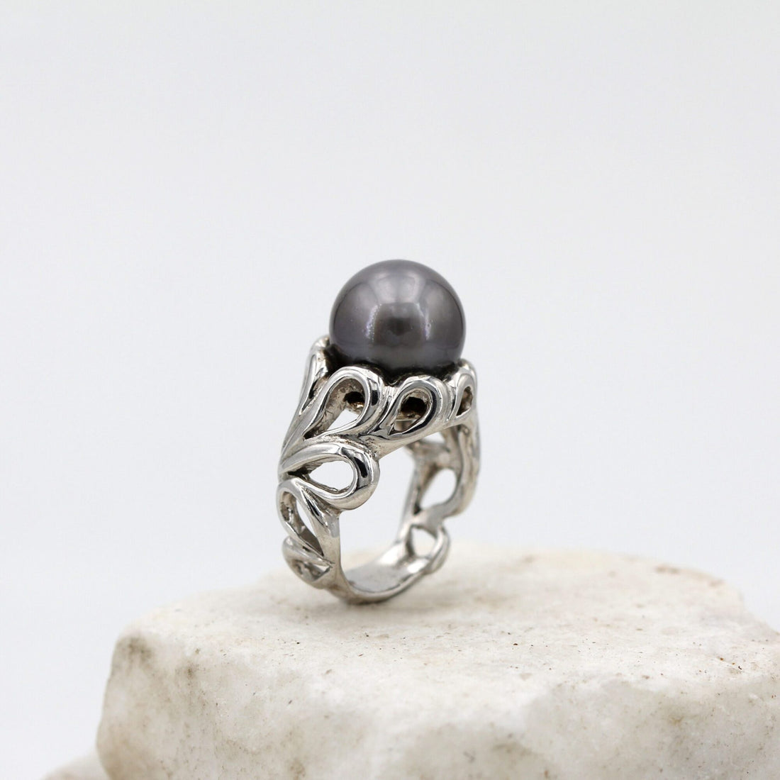 L'anello di tre quarti: la perla in cima e le volute d'argento che salgono a tenerla