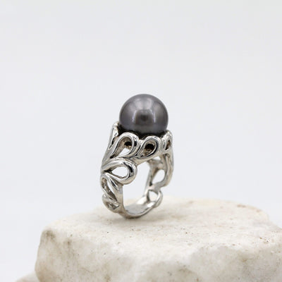 L'anello di tre quarti: la perla in cima e le volute d'argento che salgono a tenerla
