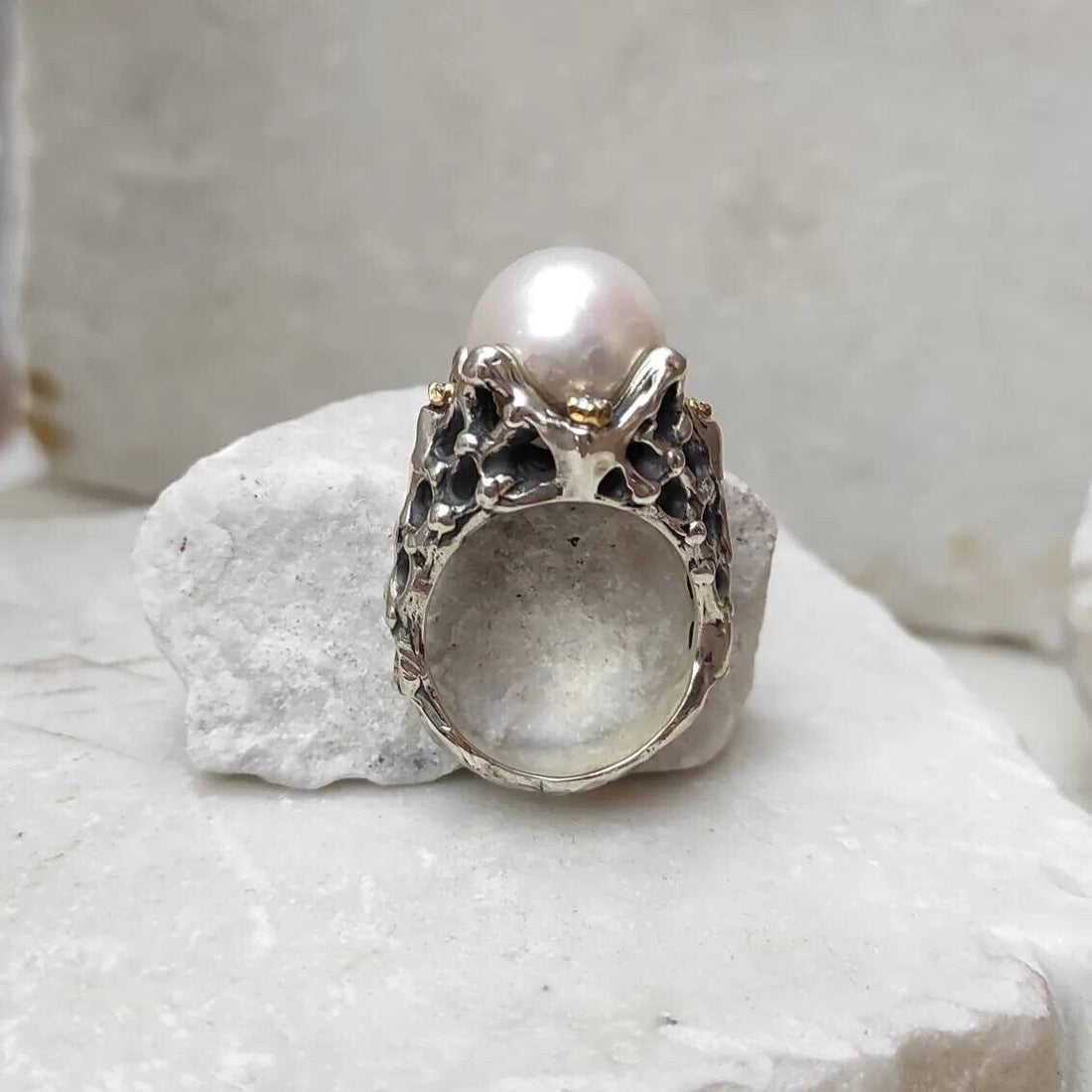 L'anello visto di fronte: la perla bianca in cima, le quattro braccia d'argento che la trattengono e la fascia forata sotto