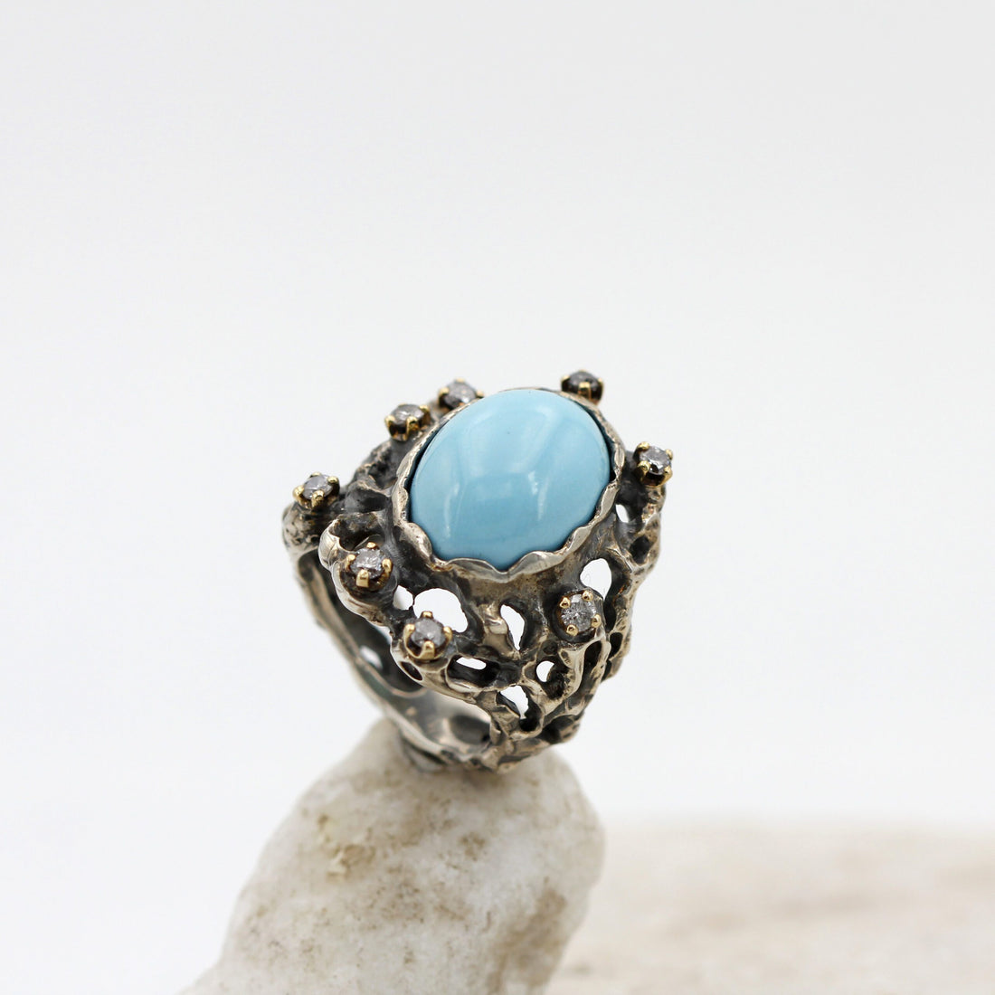The turquoise and the gold bezels of the eight diamonds seen in three-quarter view, the ring resting on a light stone
