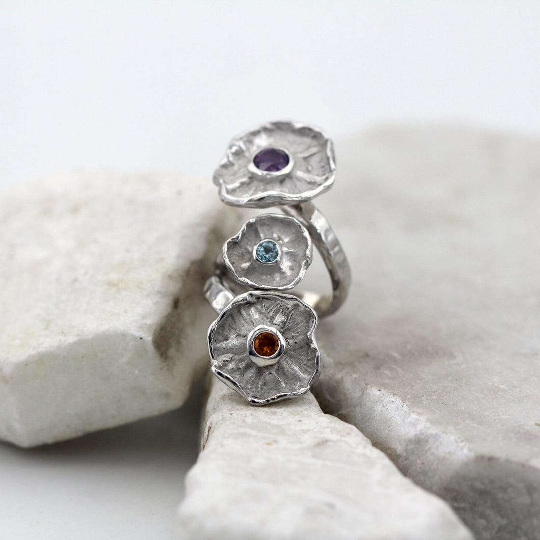 The three corollas in a row along the finger: amethyst at the top, blue topaz in the middle, citrine quartz on the largest corolla