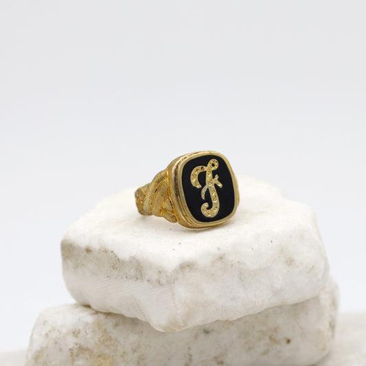 Anello da uomo in argento dorato con l'iniziale in corsivo su fondo nero, veduta di tre quarti