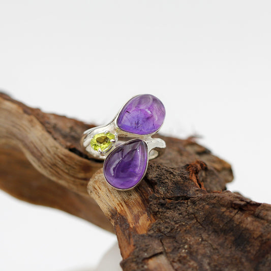 L'anello appoggiato su un ramo di legno, visto dall'alto: le due gocce d'ametista e il peridoto verde in mezzo.