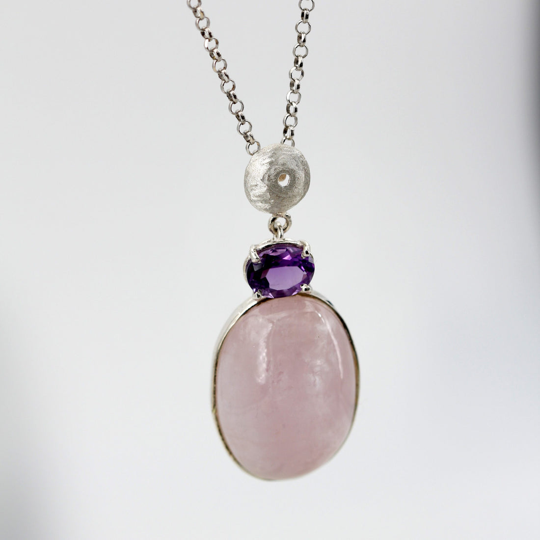 Il pendente appeso alla catena su fondo chiaro: sfera d'argento, ametista e morganite in fila