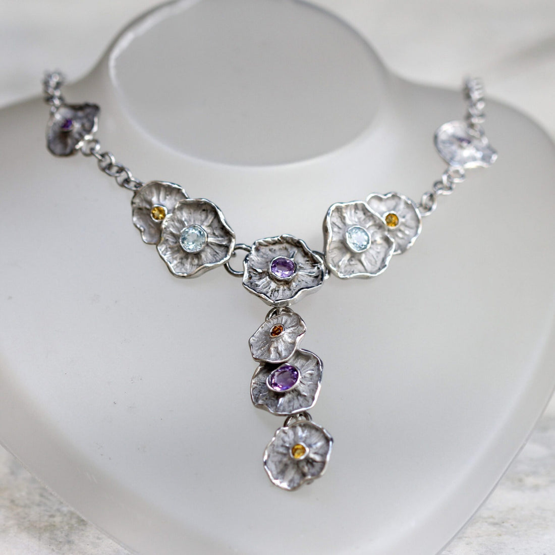The necklace worn on a bust: the row of corollas at the front and the cascade of three flowers that falls at the centre