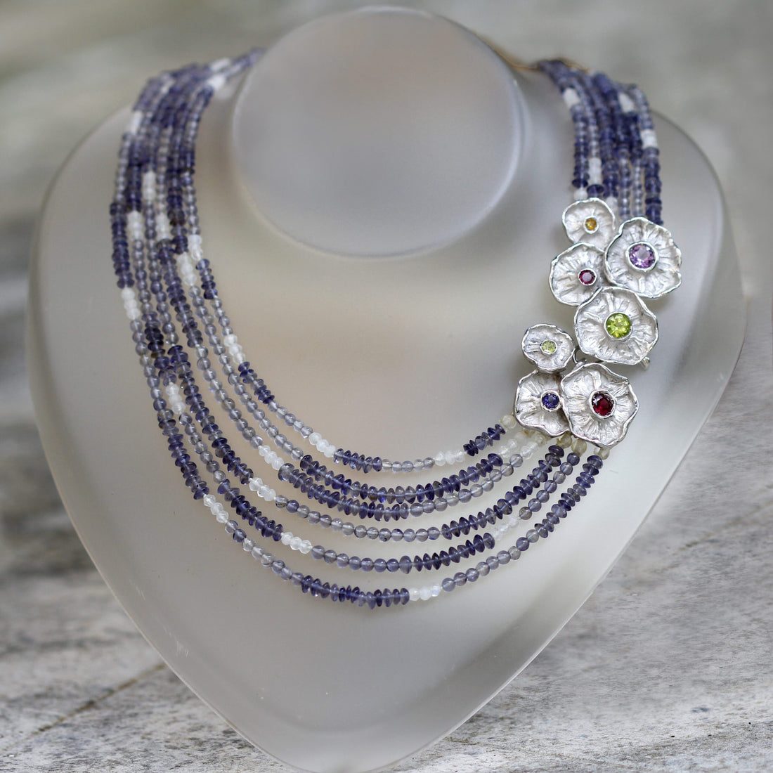 The necklace on a neck display: the six strands of iolite fall in a fan and the group of silver flowers rests to one side