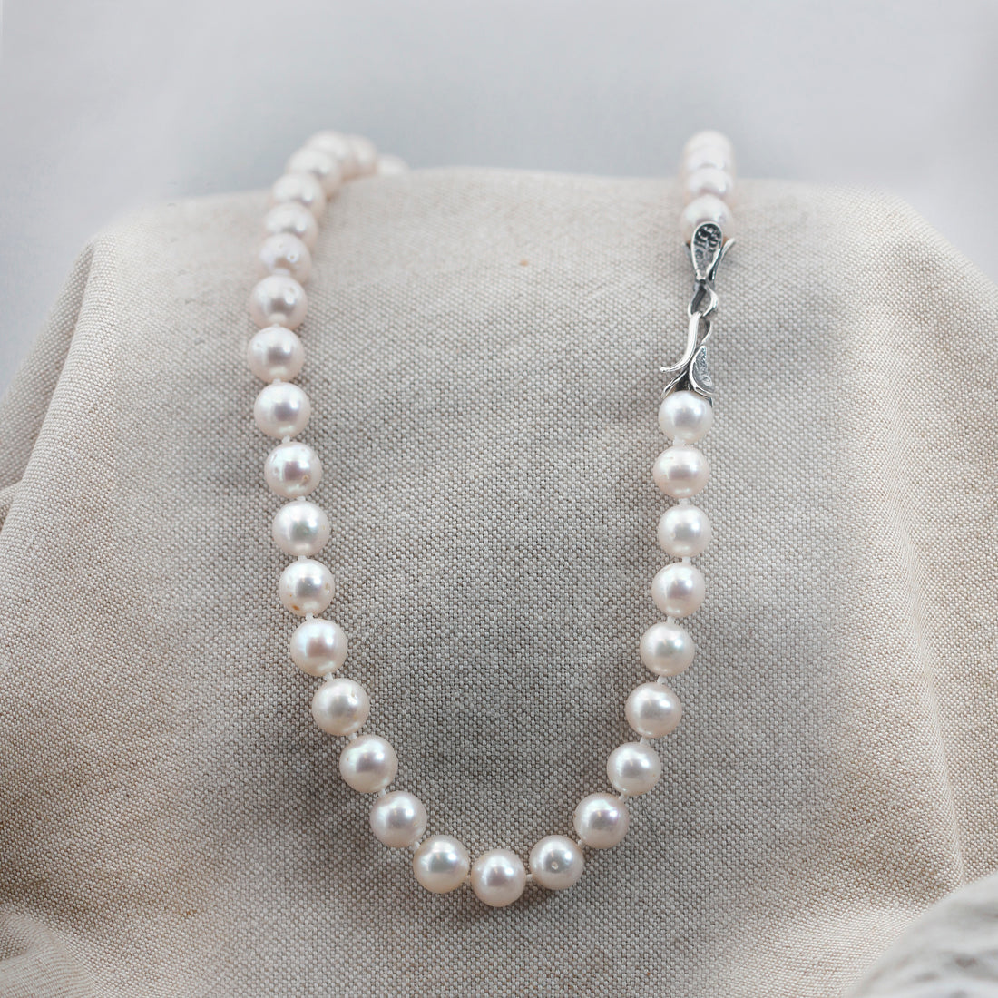 La collana distesa su tela di lino, il filo chiuso ad anello e la chiusura d'argento in alto a destra