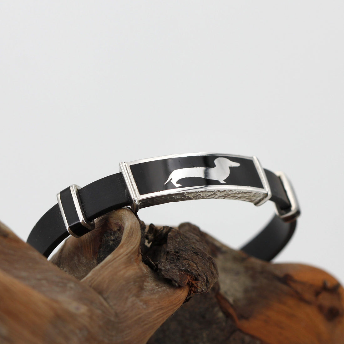 Il bracciale inarcato sopra un legno scuro, con la targhetta del bassotto in alto
