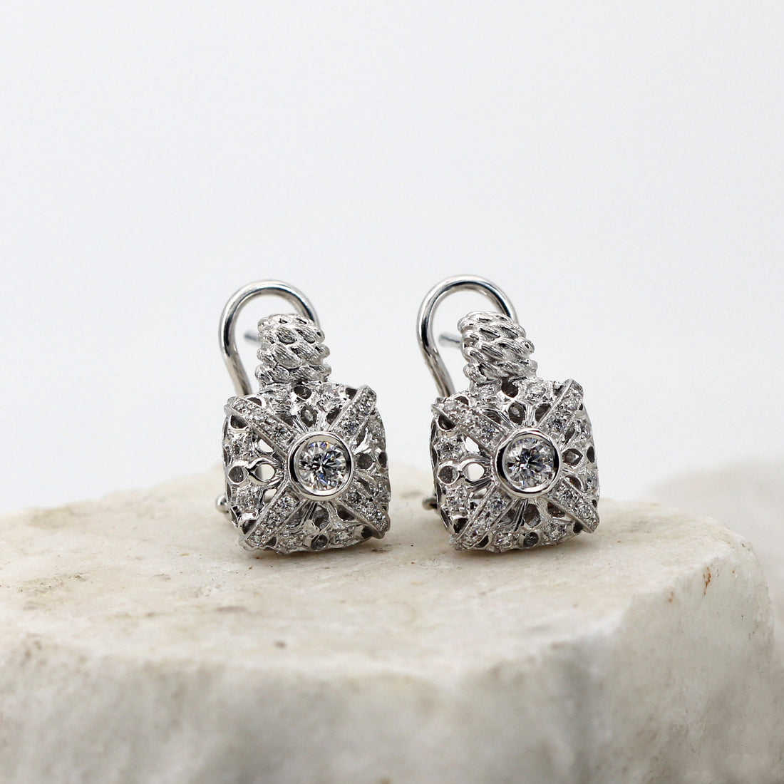 The two earrings in three-quarter view on light stone: the openwork cushion, the twisted collar and the hoop of the clasp