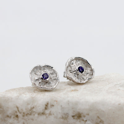 Il paio di fronte su una pietra chiara: le due corolle d'argento dal fondo sabbiato, con la iolite blu-violetta al centro di ciascuna