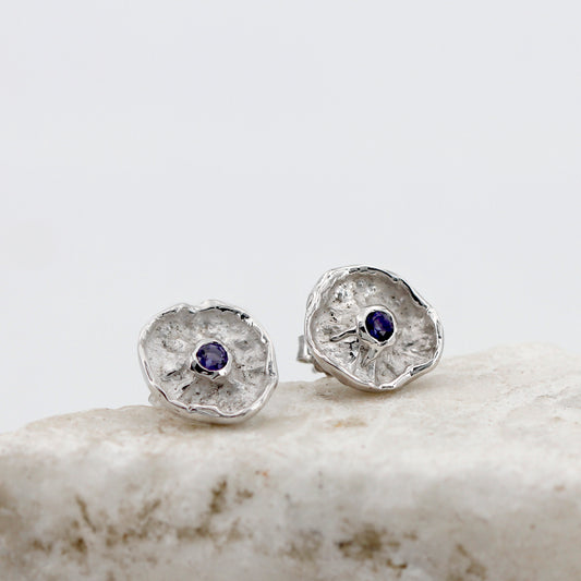 Il paio di fronte su una pietra chiara: le due corolle d'argento dal fondo sabbiato, con la iolite blu-violetta al centro di ciascuna