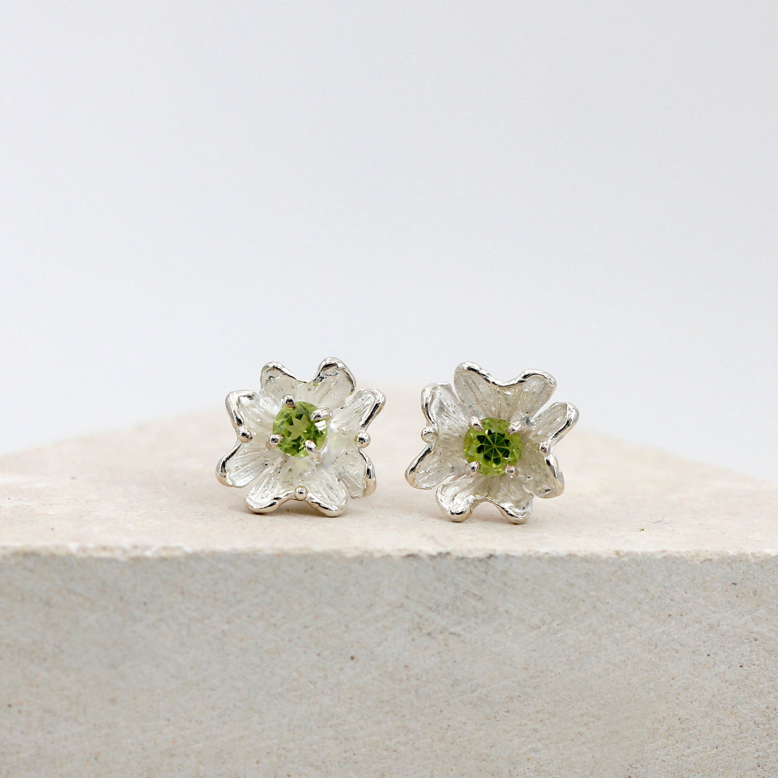 I due orecchini a fiore visti di fronte, il peridoto tondo al centro di ciascuno