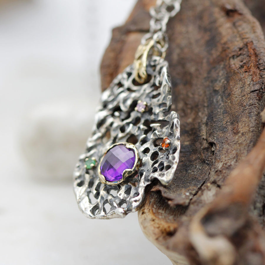 The pendant tilted on the wood: the checkerboard amethyst and the orange stone