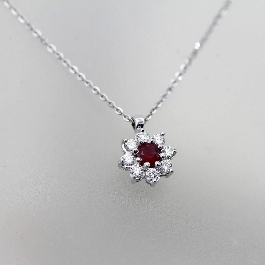 Front view on a grey background: the ruby at the centre of the eight diamonds, the chain open in a V