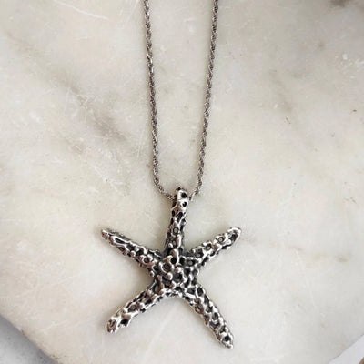 La stella marina d'argento distesa su una lastra di marmo bianco, con la catena a corda che passa nella punta del braccio in alto
