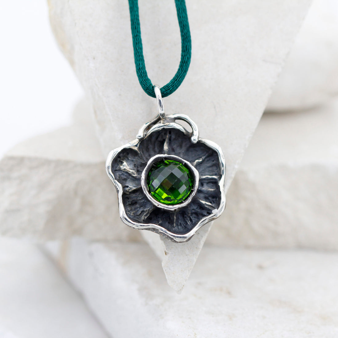 Il fiore d'argento appoggiato a una pietra bianca, con lo zircone verde al centro della corolla