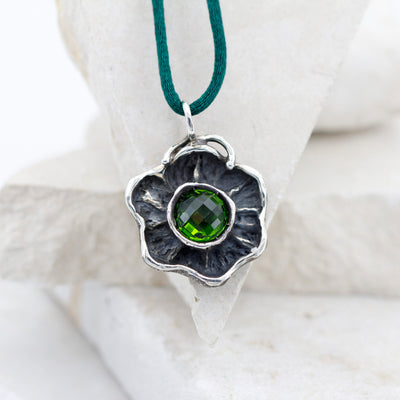 Il fiore d'argento appoggiato a una pietra bianca, con lo zircone verde al centro della corolla