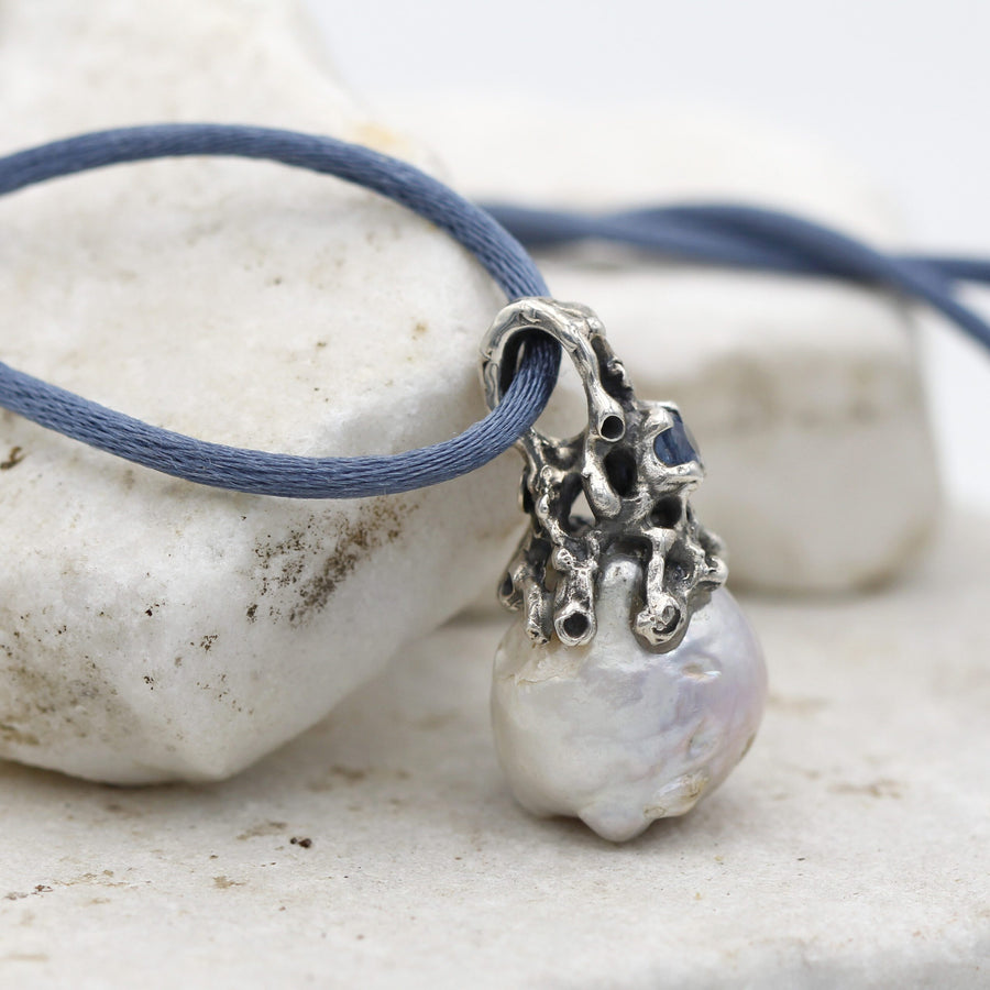 Dettaglio di profilo: le braccia d'argento che scendono sulle spalle della perla e l'anello di sospensione bucato