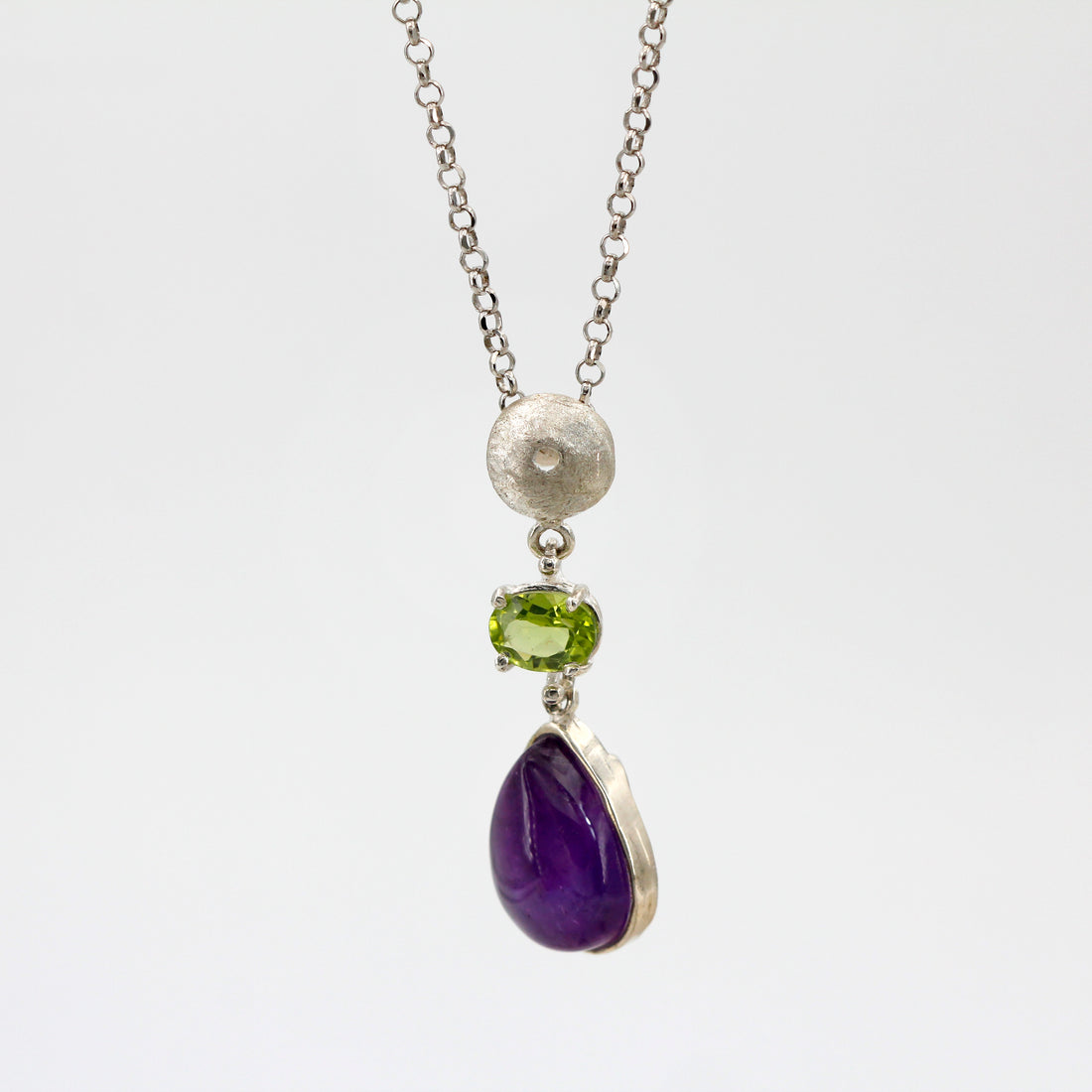 Il pendente appeso per intero: la sfera d'argento sulla catena, il peridoto verde e sotto la goccia d'ametista.