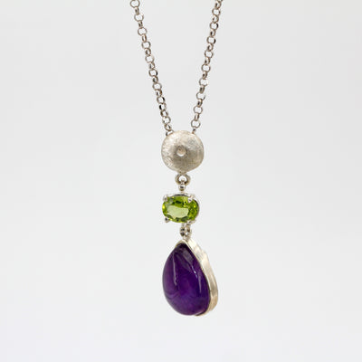 Il pendente appeso per intero: la sfera d'argento sulla catena, il peridoto verde e sotto la goccia d'ametista.