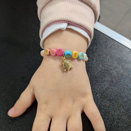 Braccialetto con le lettere VIOLA in perline colorate e ciondolo tartaruga dorato, al polso di una bambina
