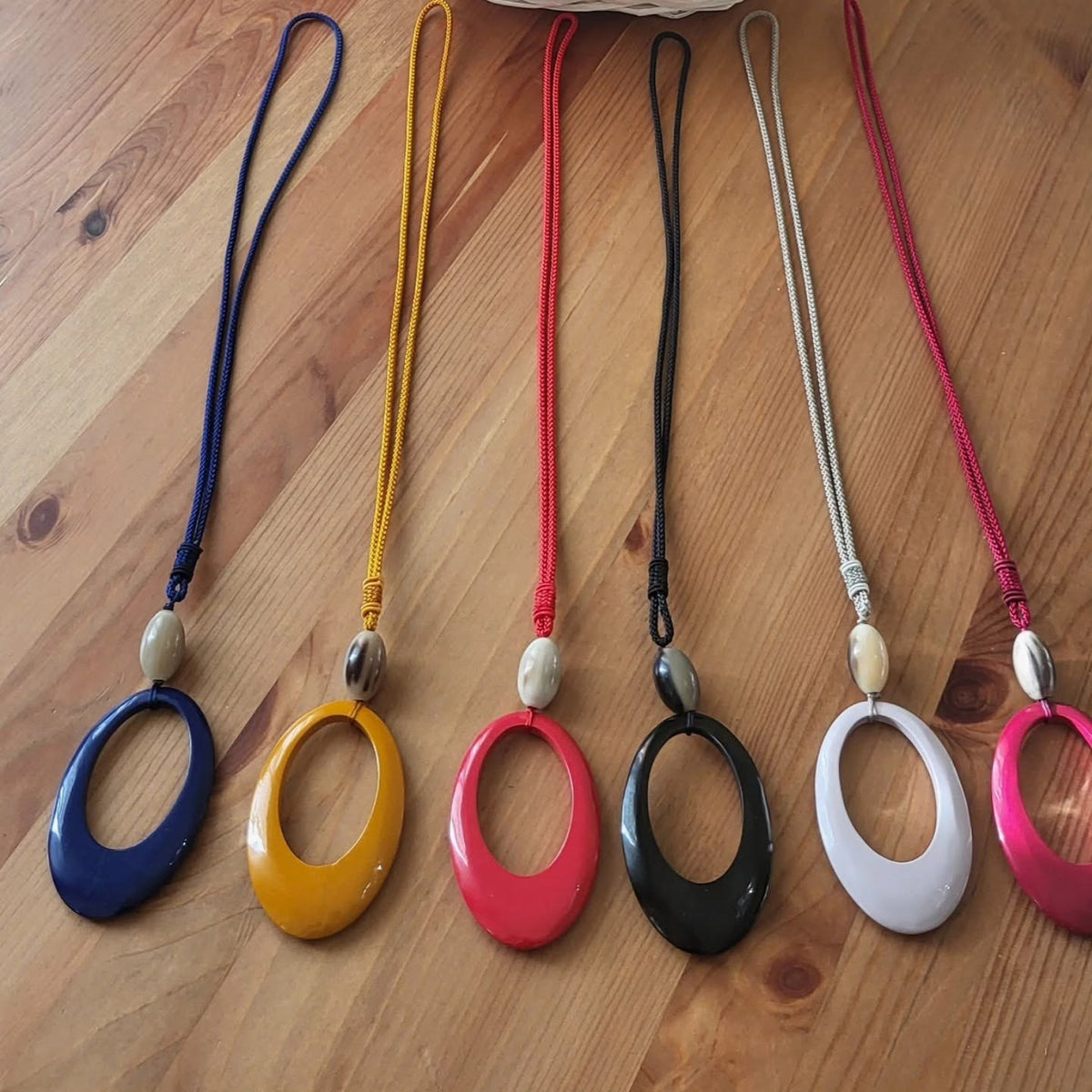 Sei ciondoli ovali su cordino intrecciato, uno per colore: blu, senape, rosso, nero, bianco e fucsia