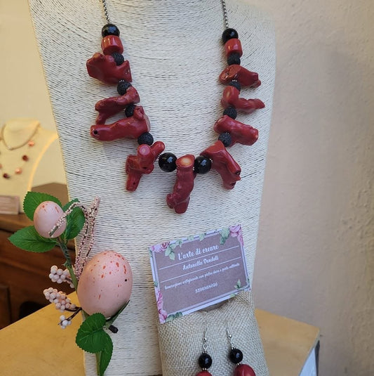 Collana di rami di corallo rosso con sfere nere e grani di lava, su un espositore di corda accanto al cartellino della bottega