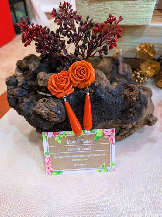 Orecchini con rosa di resina arancio al perno e goccia lunga arancio pendente, su un ceppo di legno
