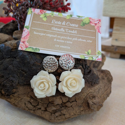 Orecchini con rosa di resina avorio e perno tondo martellato in argento, su un ceppo di legno accanto al cartellino