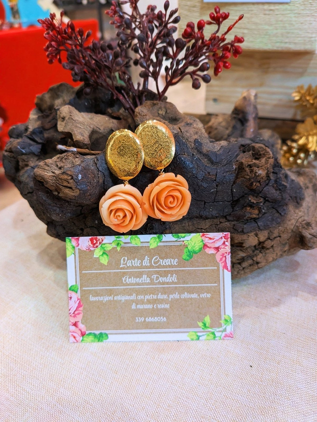 Orecchini con rosa di resina color pesca e perno ovale dorato a buccia, su un ceppo di legno