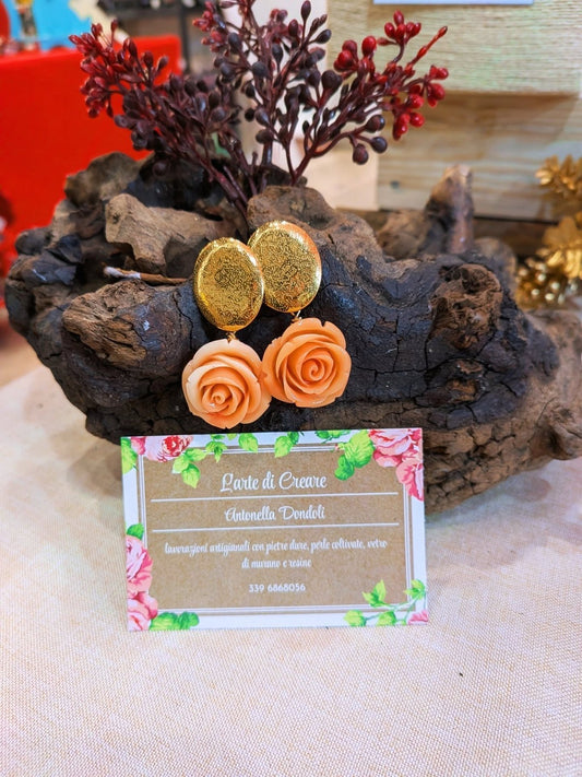 Orecchini con rosa di resina color pesca e perno ovale dorato a buccia, su un ceppo di legno