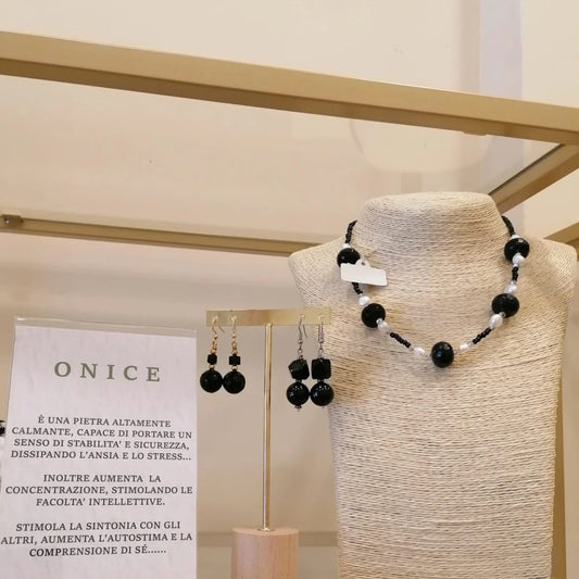 Vetrina dell’onice: girocollo di sfere di onice sfaccettato con perle bianche, due paia di orecchini e il cartoncino sulla pietra