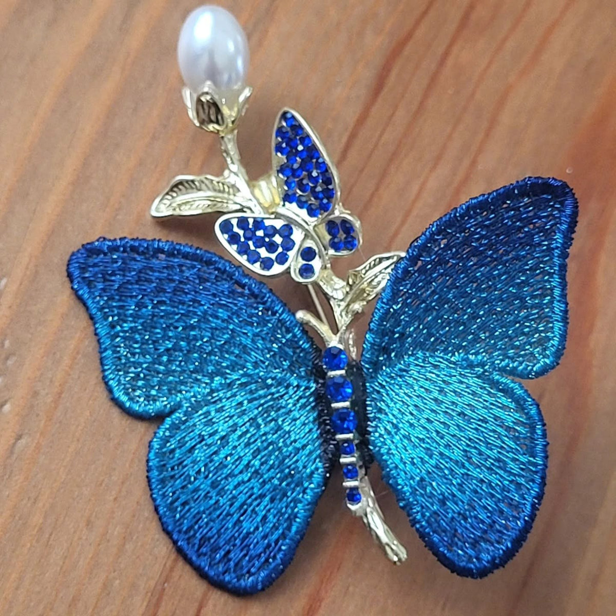 Spilla a farfalla con ali ricamate in blu elettrico, ramo dorato, farfallina di strass e perla bianca