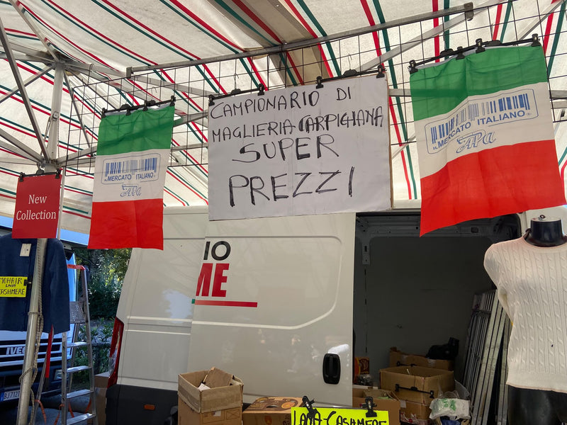 L'insegna scritta a mano del campionario di maglieria carpigiana, fra due bandiere italiane sopra il banco