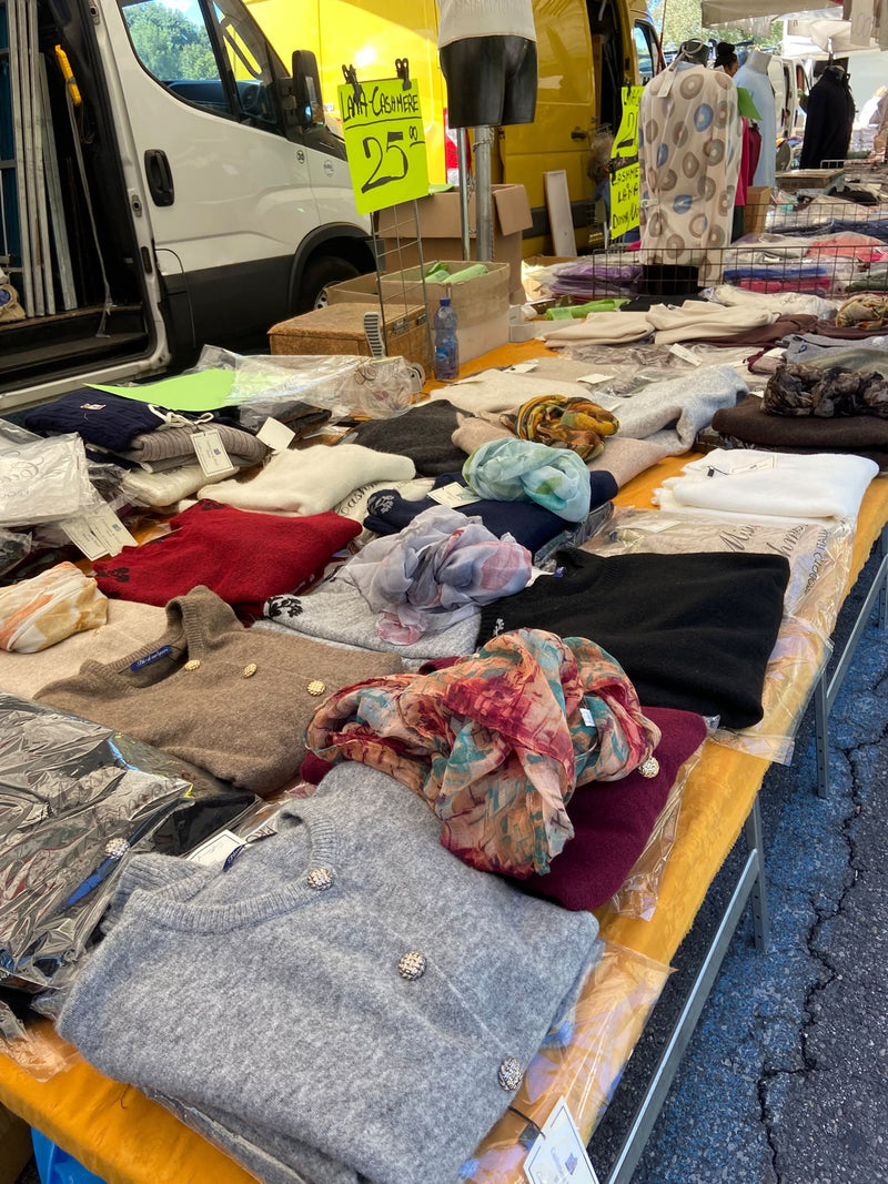 Maglioni piegati, foulard e sciarpe disposti sul banco, con il furgone dietro