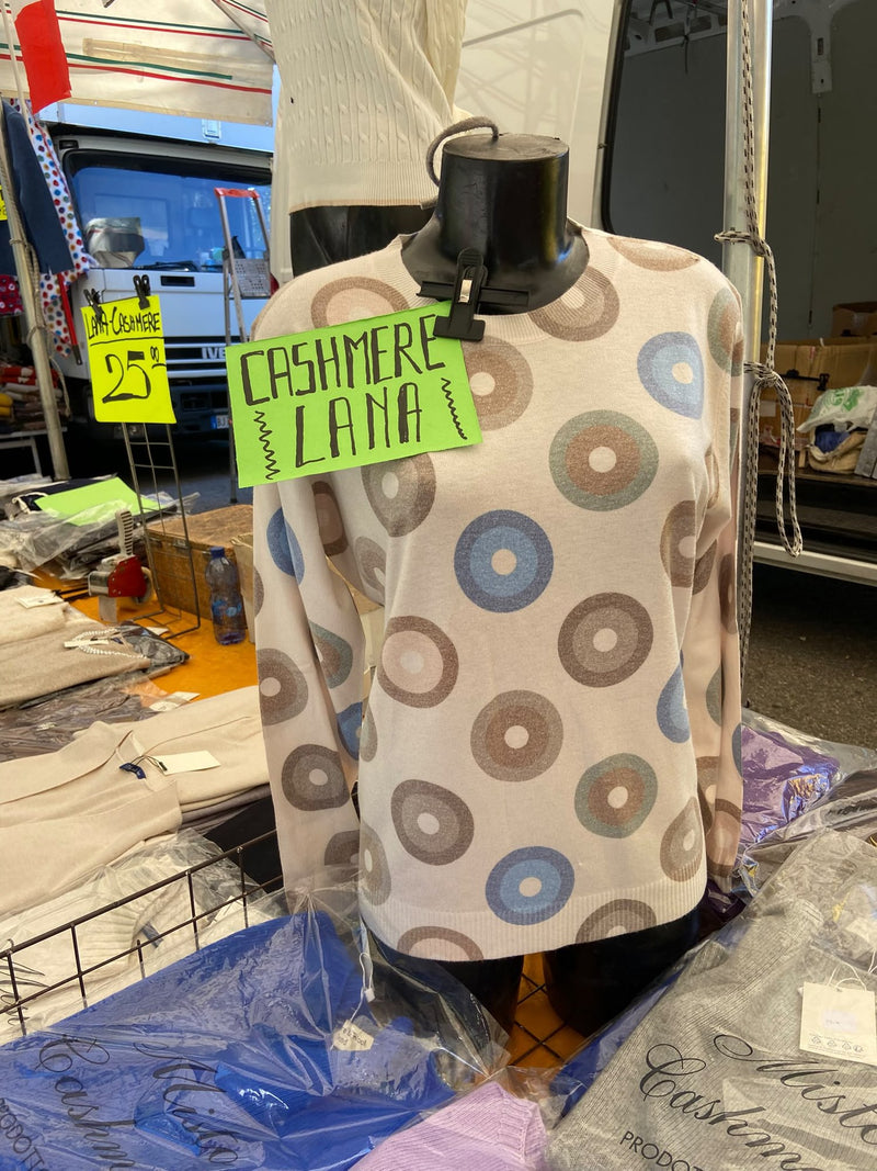 Un maglione a pois nei toni del beige e dell'azzurro su un manichino, col cartello del cashmere e della lana