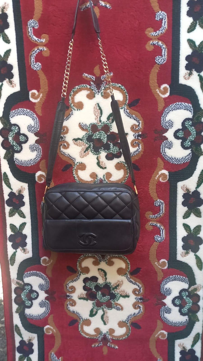 Una piccola borsa nera a catena appesa davanti a un tappeto ricamato a fiori