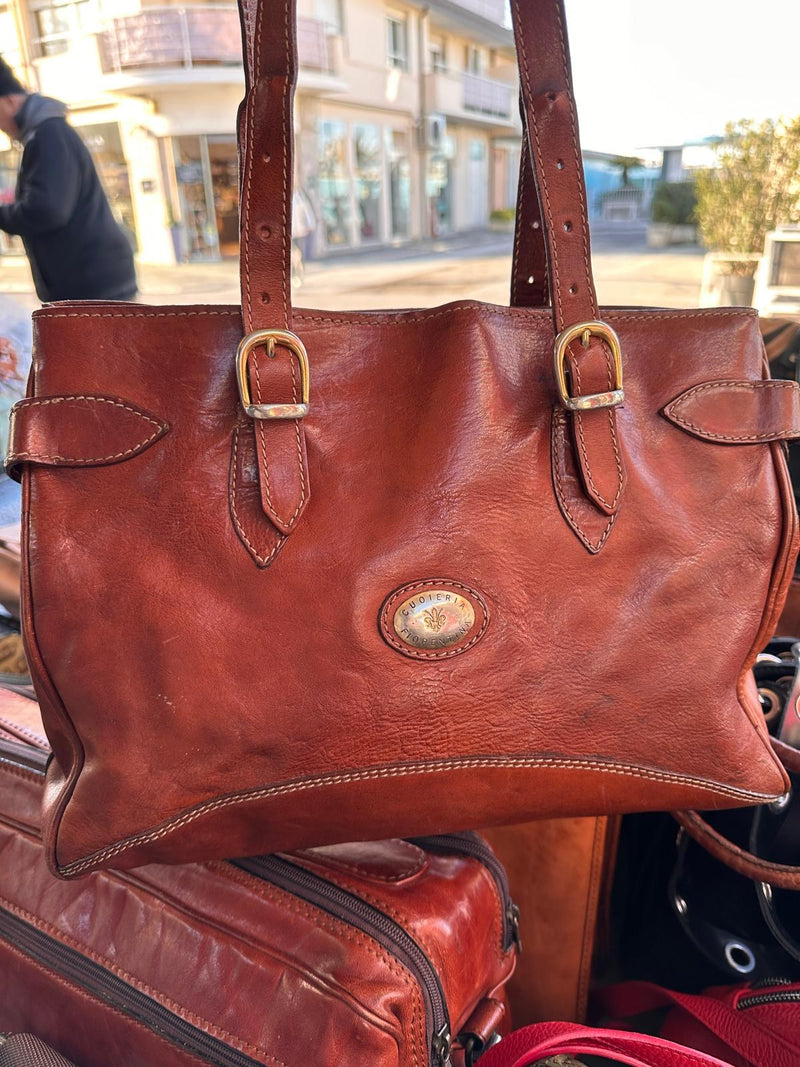 Una shopper in cuoio con le fibbie e il medaglione, appesa al banco all'aperto