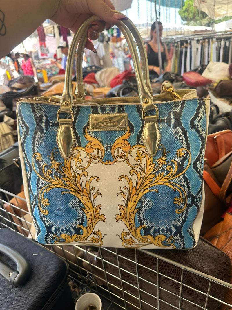 Una borsa con stampa barocca azzurra e oro e i manici in pelle, appoggiata al cesto del banco