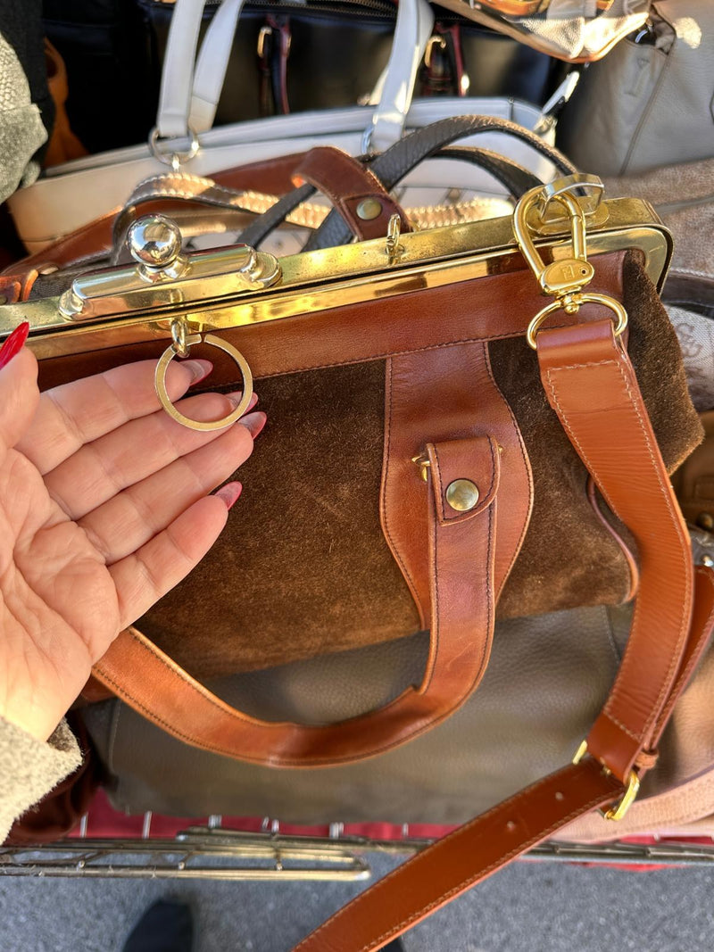 Una borsa in camoscio con la chiusura dorata a scatto, tenuta aperta sul banco