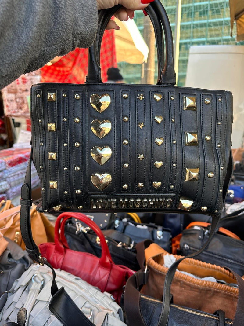 Una borsa nera con le borchie dorate a cuore, sopra le altre borse del banco