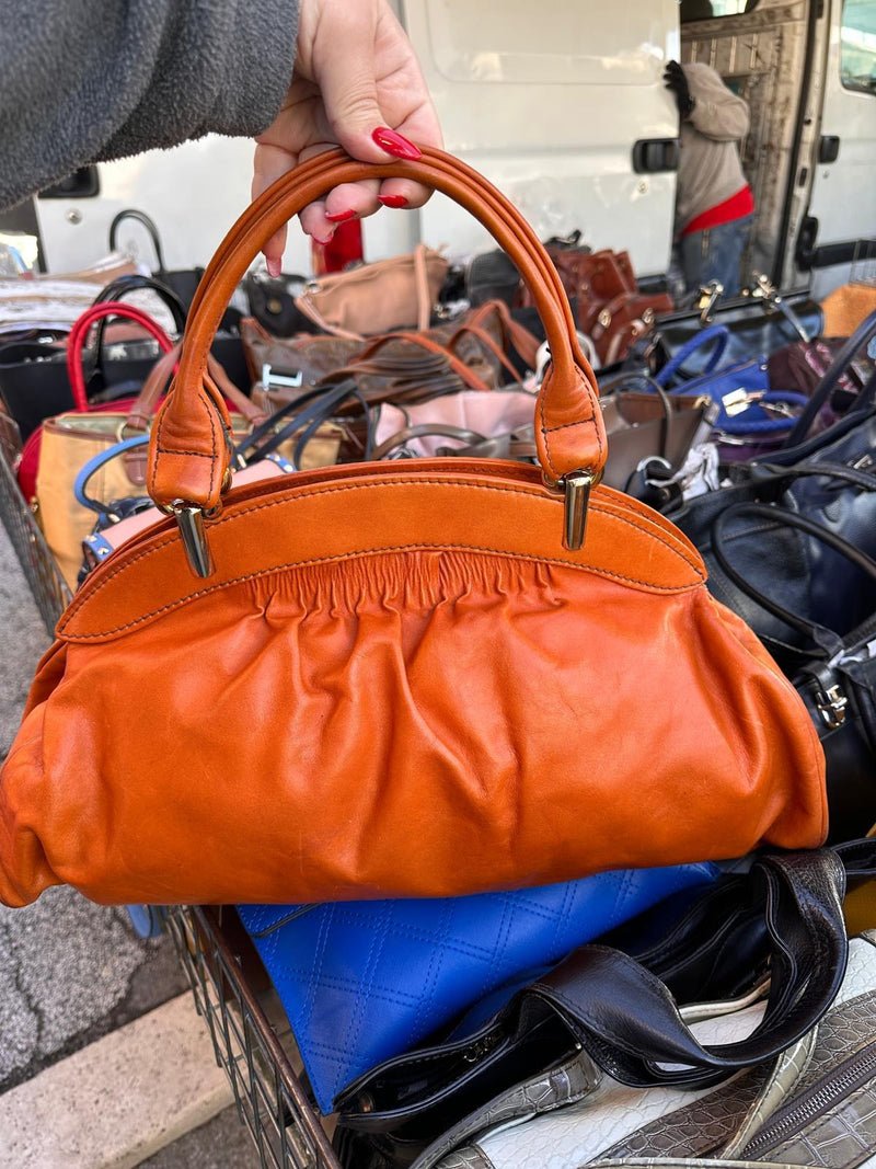 Una borsa arancione in pelle morbida, sollevata sopra il banco
