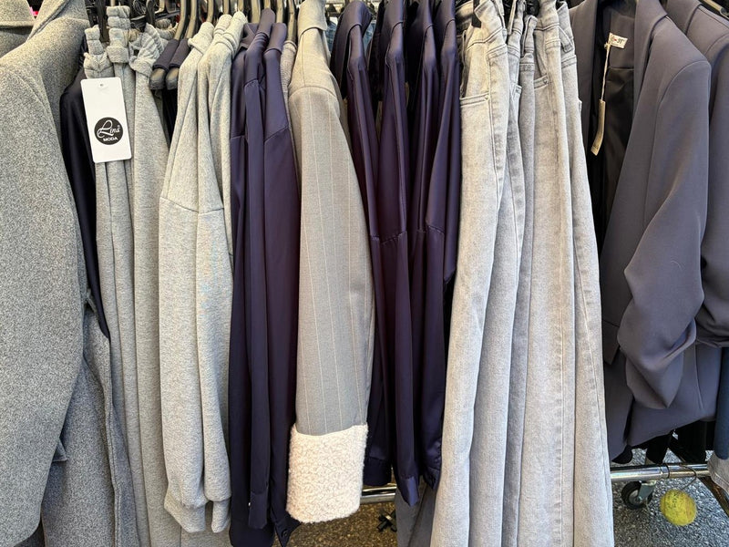 Lo stender del banco DEPES: cappotti grigi, camicie blu in raso, un blazer gessato col polsino in teddy, jeans grigio chiaro e blazer grigio-azzurri