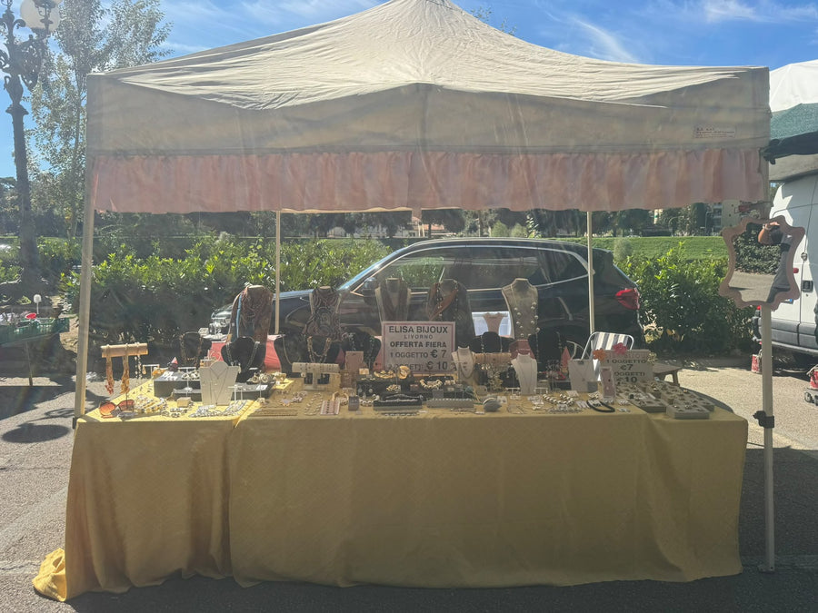 Il banco Elisa Bijoux sotto il gazebo, con l'insegna di Livorno e i collari di collane, anelli e orecchini sul telo giallo