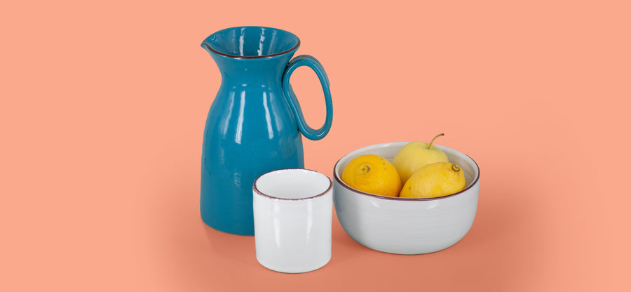 La brocca azzurro cielo accanto al bicchiere bianco neve e alla ciotola grigio perla con i limoni