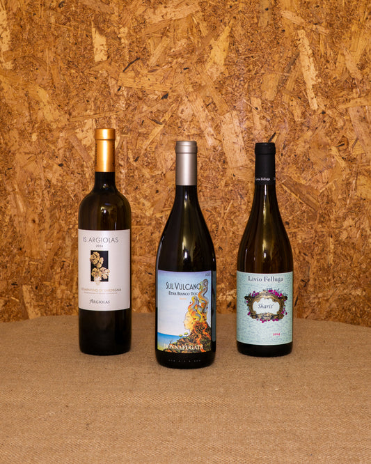 Le 3 bottiglie della selezione «Bianchi Selezione Bottegone» in piedi davanti al fondo del set: Vermentino Is Argiolas, Sul Vulcano Bianco Donnafugata e Sharis Livio Felluga.
