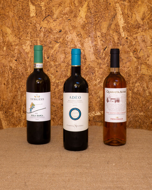 Le 3 bottiglie della selezione «Pranzo di Natale Toscano» in piedi davanti al fondo del set: Vernaccia Isola Bianca, Bolgheri Adeo e Vin Santo Quaranta Altari.