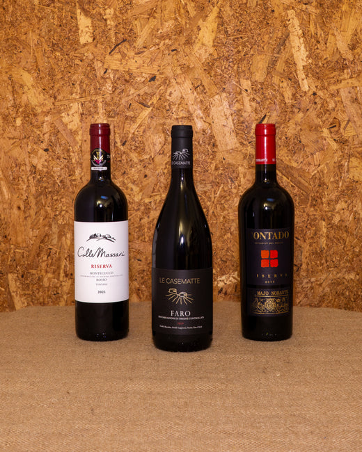 Le 3 bottiglie della selezione «Rossi d’Autore» in piedi davanti al fondo del set: Montecucco Riserva ColleMassari, Faro DOC Le Casematte e Aglianico del Molise Contado Riserva.