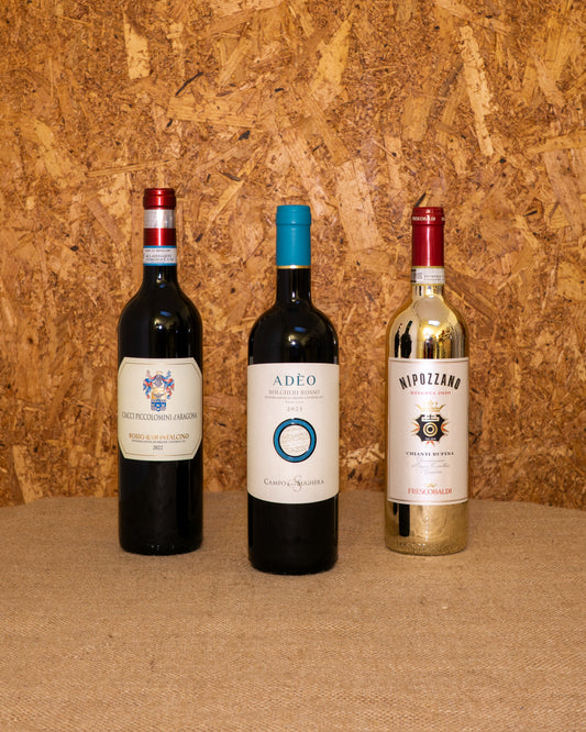 Le 3 bottiglie della selezione «Toscana DOC» in piedi davanti al fondo del set: Rosso di Montalcino Ciacci Piccolomini, Bolgheri DOC Adeo e Chianti Rufina Nipozzano.